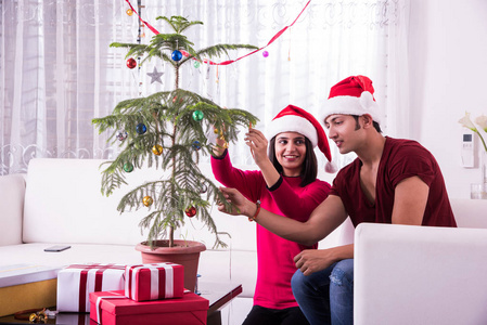 年轻的印度夫妇放圣诞球或上绿树铃在一起，印度庆祝圣诞节或圣诞装饰圣诞树