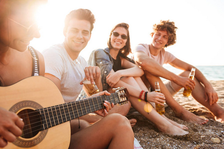 一群快乐的年轻朋友一起在沙滩上玩耍, 喝啤酒, 在野营时弹吉他。