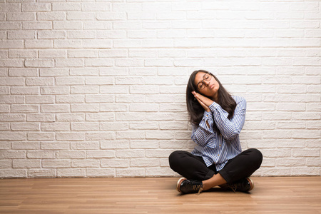 过度捕捞印度年轻的印度妇女坐在砖墙上疲惫而困倦, 看起来舒适而轻松