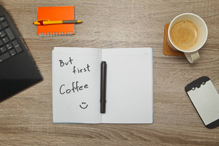 带有文本，但第一咖啡打开笔记本和一杯咖啡上木制的背景。自上而下的视图