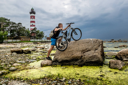 骑自行车的人将他的自行车推一块巨大的岩石，在背景 Shepe