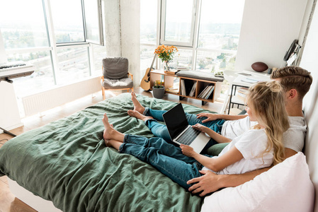 年轻夫妇的侧面观看与数字笔记本电脑与空白屏幕休息在家里的床上