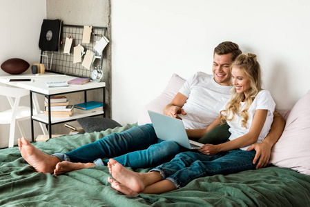 微笑的年轻夫妇与数字笔记本电脑休息在家里的床上
