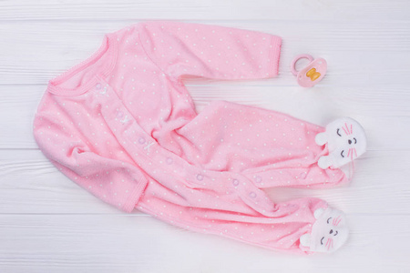粉红色婴儿脚睡衣和奶嘴。白色木材背景