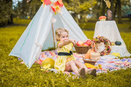 小女孩躺在帐篷里玩耍, 孩子们的房子在公园里的帐篷里, 秋天可爱的卷发女孩的肖像。收获或感恩。秋天的装饰, 聚会, 野餐。穿黄色