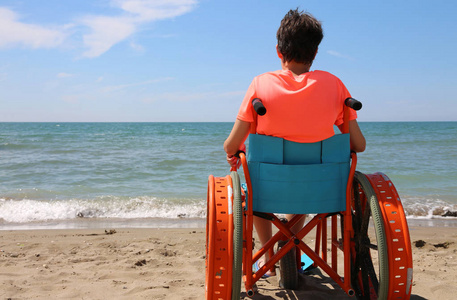 在海边海滩上带着金属轮子的特殊轮椅上的男孩