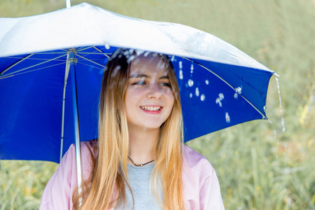 年轻女子站在蓝色的伞下在雨中