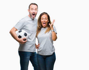 中年西班牙裔夫妇举行足球足球在孤立的背景非常高兴和兴奋, 获胜者的表情庆祝胜利尖叫着与灿烂的笑容和举起的手
