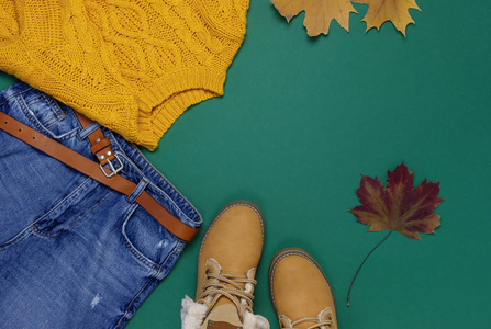 女性橙色针织毛衣, 蓝色牛仔裤, 靴子和秋叶绿色背景背景景观平躺式时尚女士服装集时尚舒适针织秋季配件女性时尚造型