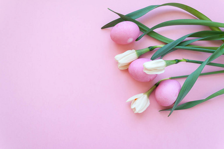 美丽的白色水仙与五颜六色的鸡蛋在浅粉红色的背景。具有复制空间的春季和复活节假日概念