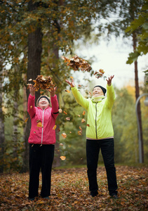 在秋季公园里, 老妇人向空中扔树叶。微笑。全身