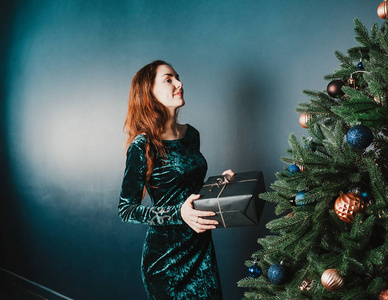美丽的女孩与圣诞树附近的礼物盒, 面带微笑。新年和圣诞节装饰的概念。豪华绿色, 蓝色, 金色。家庭和家庭的温暖。节日主题横幅