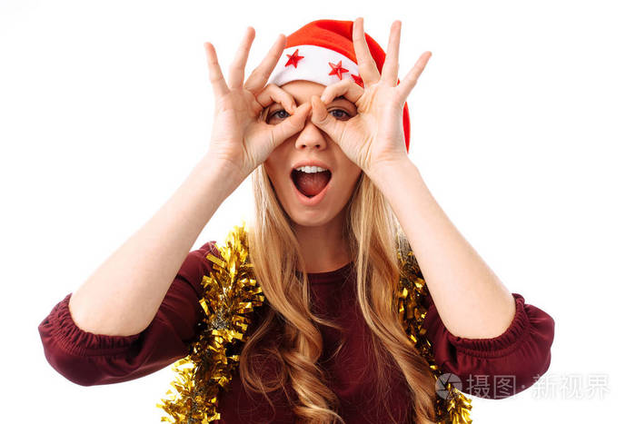 一个美丽的年轻女子戴着圣诞老人的帽子, 用手指在白色背景上做眼镜手势的肖像。圣诞节