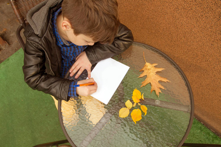 男孩在写东西。男孩在户外做作业。男孩在纸上画画或写信