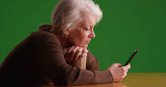 在绿色屏幕上使用智能手机的悲伤的白人老年妇女的配置文件
