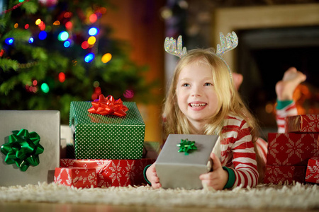 快乐的小女孩，穿着圣诞睡衣在圣诞前夜在舒适的黑暗客厅的壁炉旁玩。在家里庆祝圣诞节