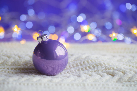 淡紫色圣诞球在白色针织面料在紫色背景与温暖的 bokeh。新年贺卡。圣诞装饰