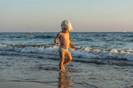 微笑小宝贝男孩在沙滩上在日落时运行时溅起水花在海