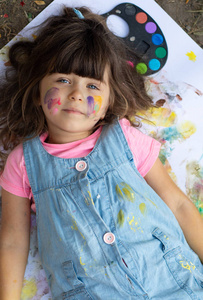 有趣的小女孩与彩色的脸使用水彩画。愉快的孩子享受艺术和工艺绘画与他的手