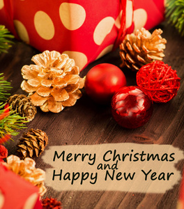 圣诞节和元旦节日装饰, 红色和金色的球, 五颜六色的冷杉锥和分支与礼物包裹在红色的纸与金色的圆圈在棕色木头背景。从上面看文字圣诞