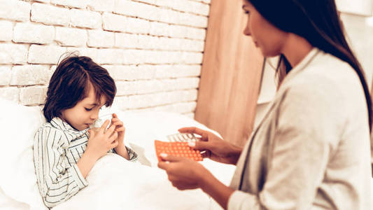 关心妈妈给生病的男孩丸.担心的母亲给生病的孩子一杯水.医院理念.