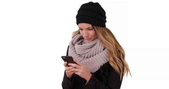 妇女在舒适的帽子和围巾短信与移动设备在白色背景