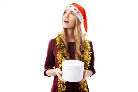 沉思的年轻女子, 戴着圣诞老人的帽子, 梦着, 望着身边, 在她的手中, 一个白色背景的礼品盒。圣诞节