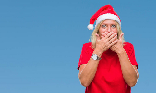 中年金发女子戴着圣诞节帽子在孤立的背景震惊地覆盖嘴与手错误。秘密概念