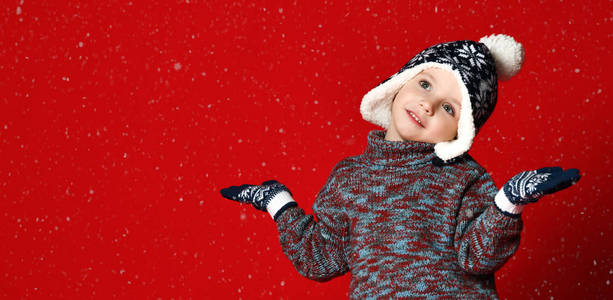 戴着帽子的可爱的小男孩, 戴着浮夸和手套, 手臂伸向一旁, 捕捉雪花