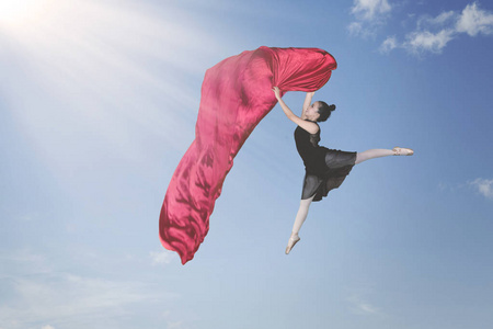 女性芭蕾演员在蓝天上跳行时, 用红色面料跳舞的照片