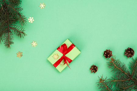 圣诞装饰。礼品盒, 冷杉树枝与锥和装饰雪花在绿色的背景。顶部视图。圣诞贺卡概念