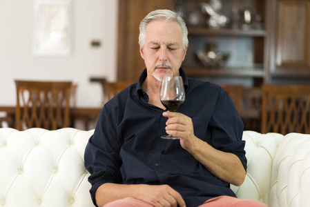 一个成熟的人的肖像在家里享受一杯葡萄酒红酒
