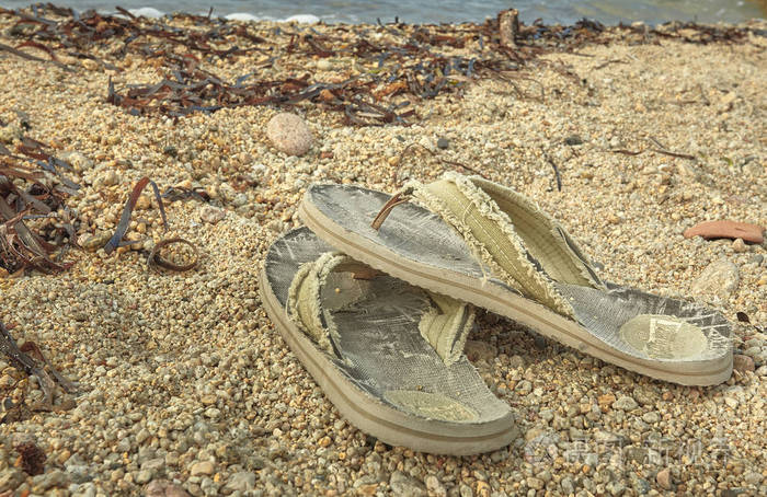 一对破旧的人字拖被遗弃在地中海海滩的沙滩上