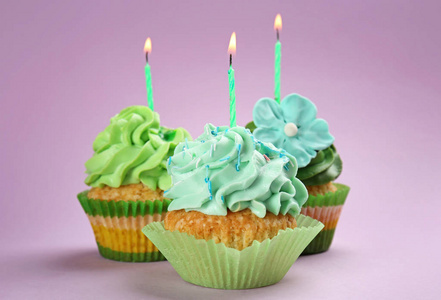 美味的生日纸杯蛋糕与燃烧的蜡烛在颜色背景