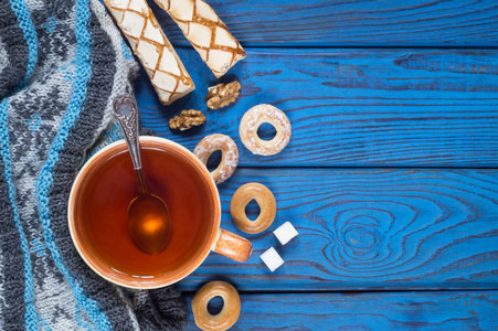 在蓝色木桌的背景下, 一杯茶一条针织围巾和百吉饼