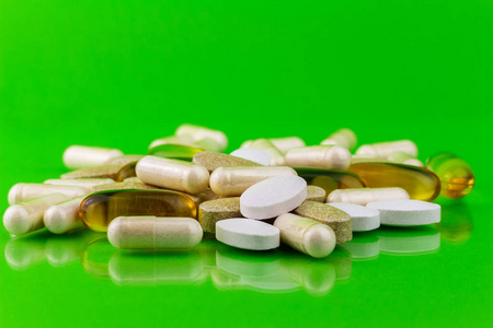混合的天然食品补充药片，欧米茄 3，钙，维生素和氨基葡萄糖胶囊对绿色背景