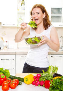 微笑着的年轻女人，在现代的厨房里吃新鲜的沙拉