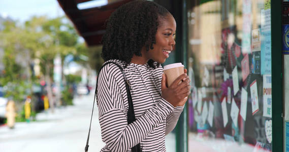 可爱的黑人妇女在条纹顶部喝咖啡, 看着窗口显示