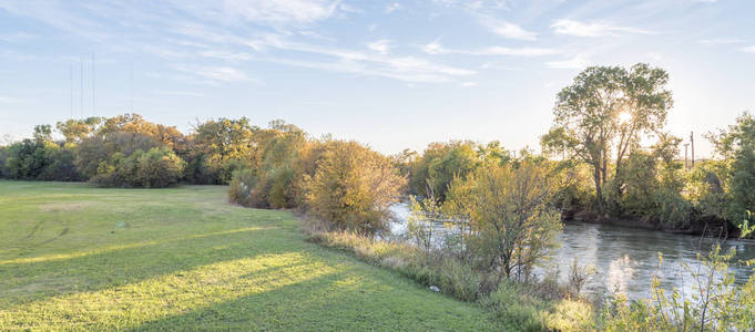 全景美丽的河边公园与秋天的树叶充满活力的颜色和太阳窥视通过树木在卡罗尔顿, 得克萨斯州, 乌萨。日落时令人惊叹的黄色秋叶