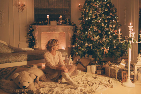 圣诞节的晚上。年轻美丽的金发女子，在经典公寓白色壁炉装饰树