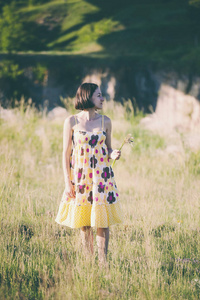 一个女孩采摘野花。穿着夏装的女人正沿着田野走。小穗的花束。女性手撕掉植物。草甸花
