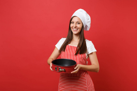家庭主妇女厨师或面包师在条纹围裙, 白色 t恤, 扭矩厨师帽查出的红色墙壁背景。管家妇女持有金属烘焙形式的馅饼。模拟复制空间概念