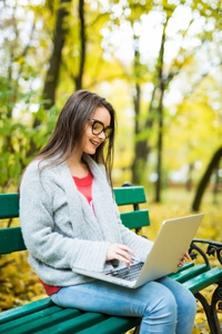 秋天的公园在笔记本电脑上工作的女大学生