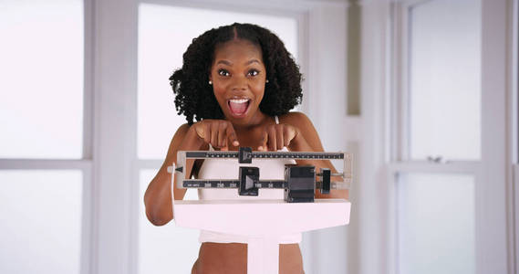 迷人的微笑的黑人妇女欢呼减肥的减肥愉快地指向规模