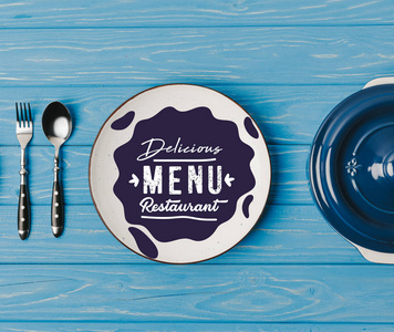 在蓝色桌子上的叉子, 勺子和盘子的顶部视图, 美味的菜单餐厅字母