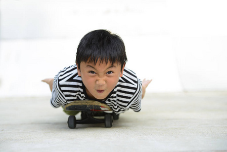 滑稽的亚洲男孩躺在滑板上寻找相机