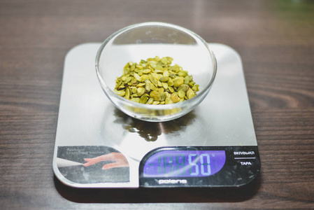 与五十克的绿色南瓜种子在厨房称重机在一个黑暗的木桌上的玻璃碗