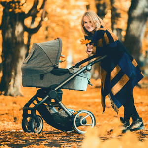 一个年轻母亲与婴儿小推车走过秋天的公园