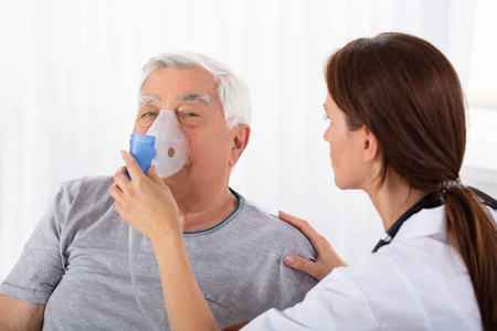 年轻的女医生持有氧气面罩在高级男性患者的脸上