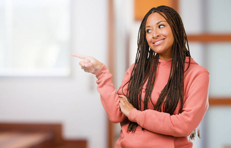 一个年轻的黑人妇女的肖像, 她戴着辫子指着侧面, 微笑着惊讶地呈现的东西, 自然和休闲